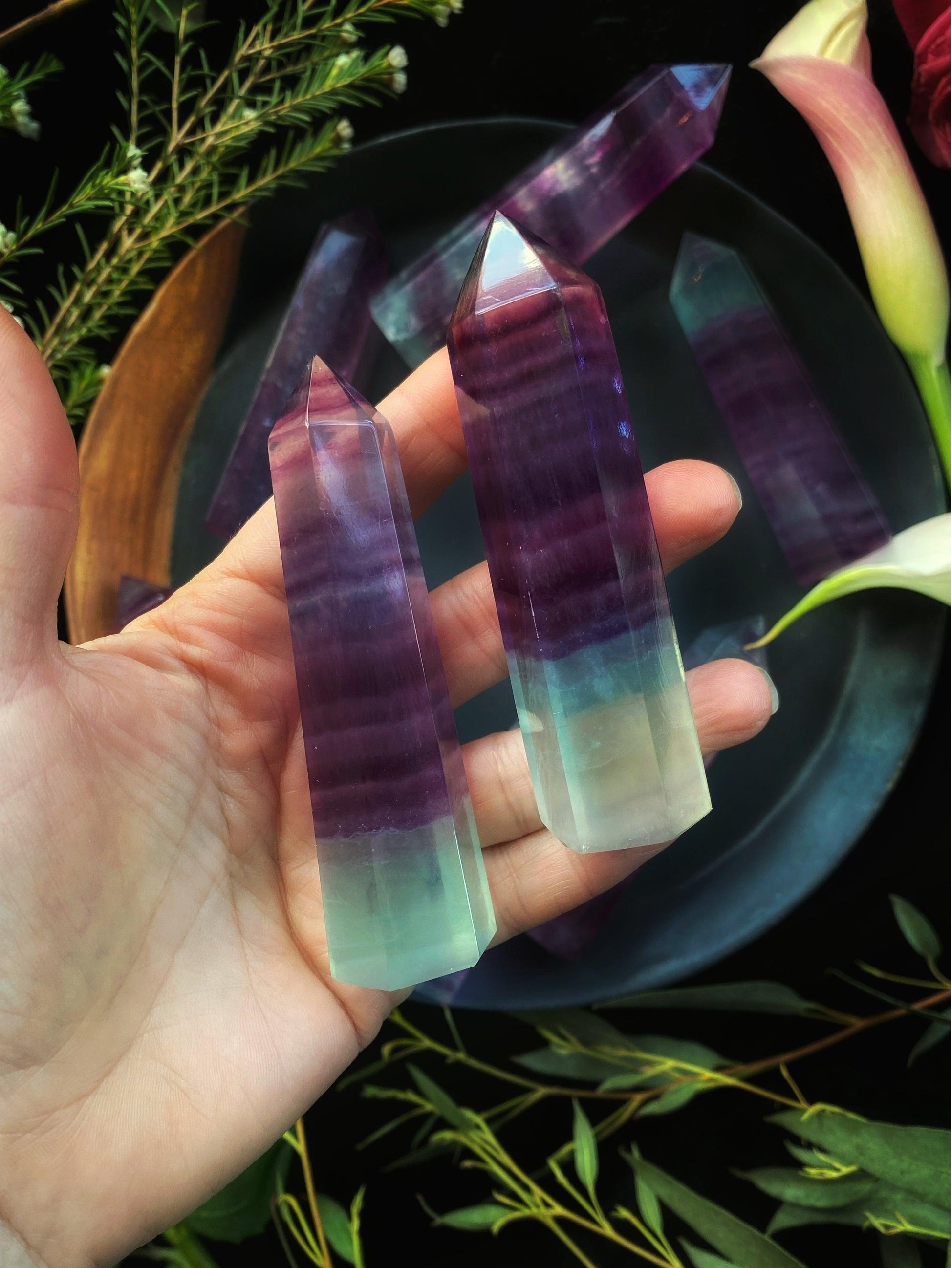 Hand holding two colorful crystal sticks with a natural background