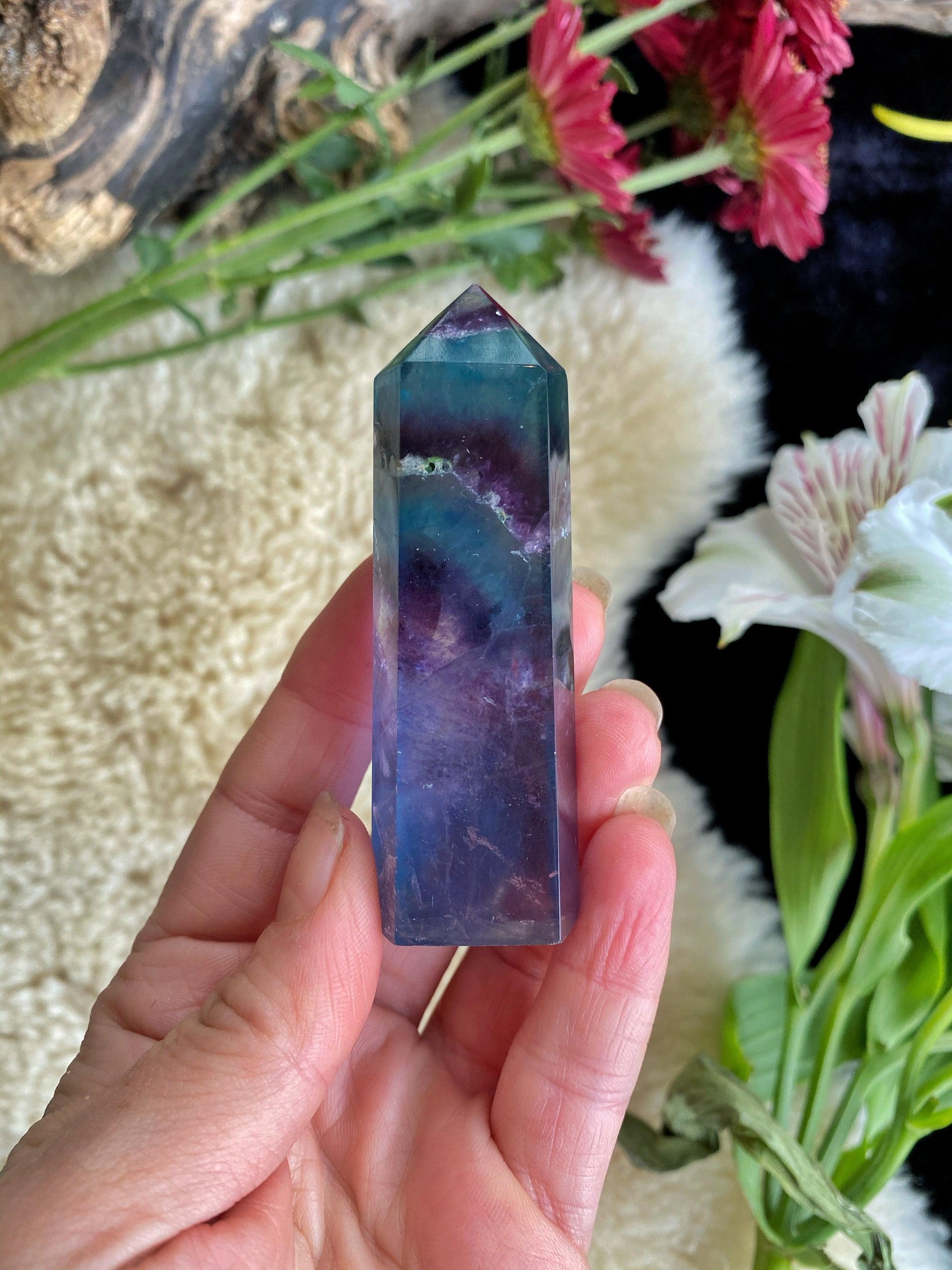 Hand holding a multicolored crystal with flowers and a textured surface in the background