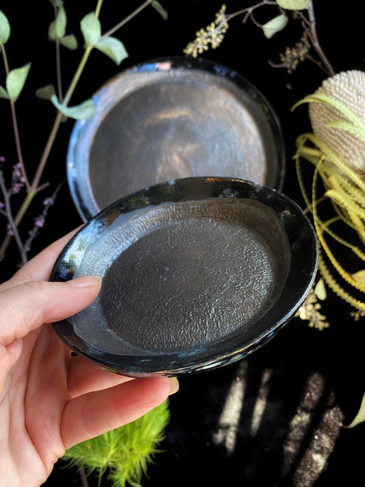 Person holding a black cast iron skillet against a dark background with greenery.