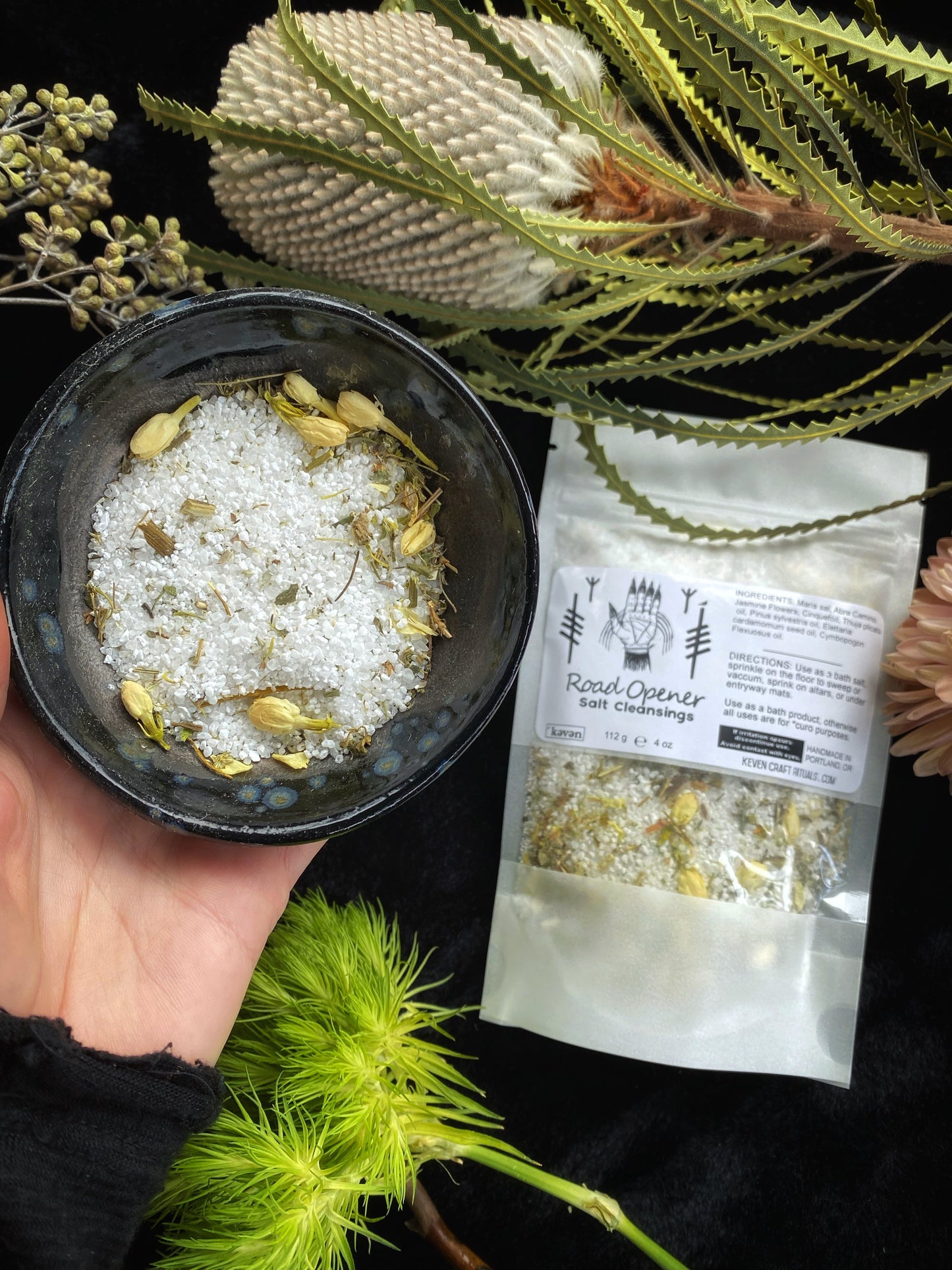 Hand holding a small black bowl with white powder and yellow flowers, next to a package labeled 'Floral Corner'.