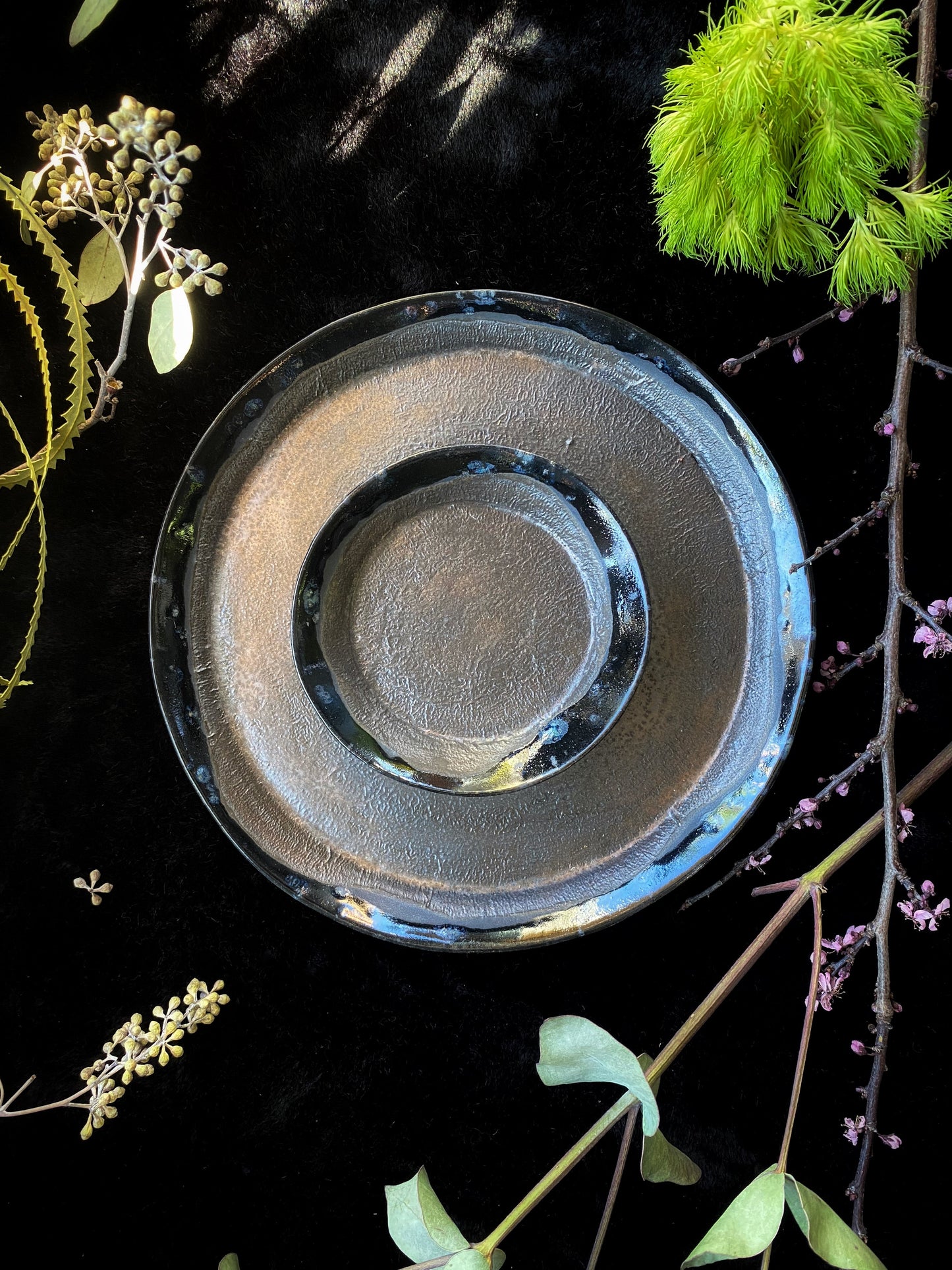 Stack of ceramic plates on a dark surface with greenery