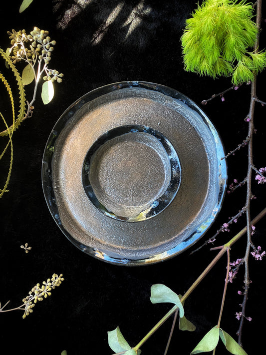 Stack of ceramic plates on a dark surface with greenery