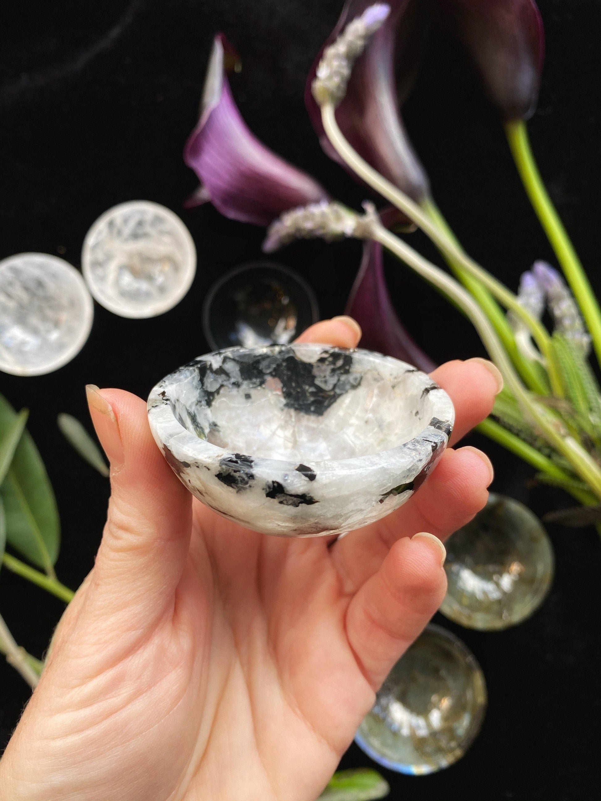 Hand holding a small, decorative crystal bowl with purple flowers in the background