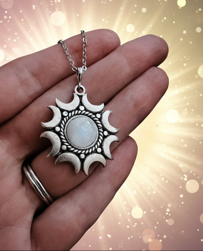 Silver sun and moon pendant necklace held in a hand against a dark background