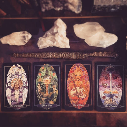 Four tarot cards with ornate illustrated designs are arranged on a dark wooden surface, with crystals and a decorative object placed above them.