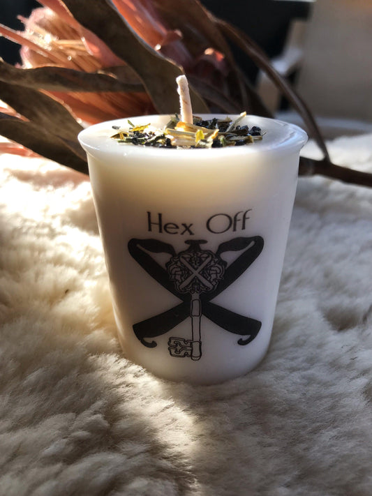 Candle in a white container with 'Hex Off' text and design on a fluffy surface