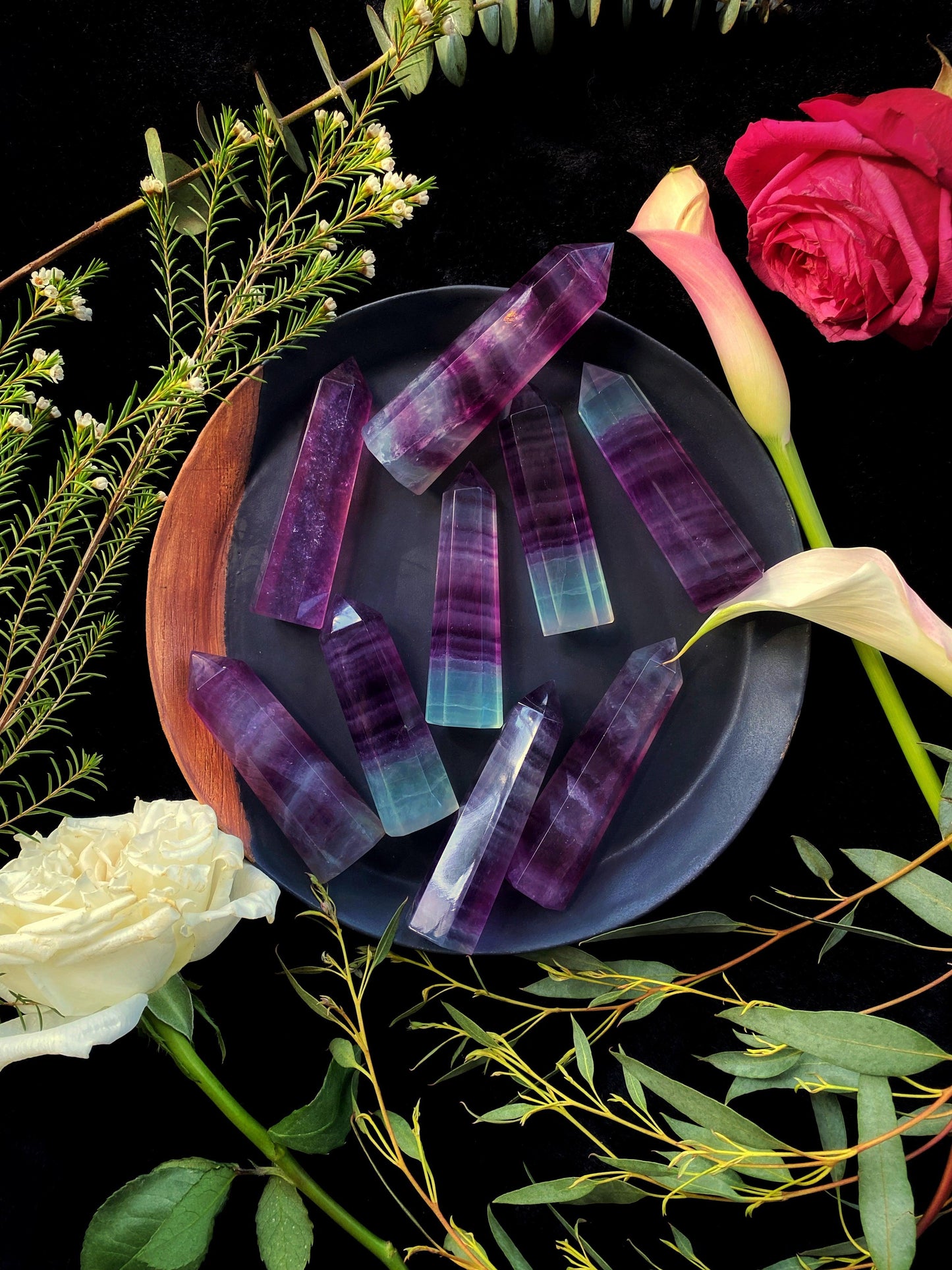 Colorful crystal-like objects on a dark surface with flowers and greenery around.