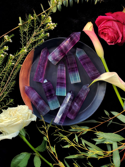 Colorful crystal-like objects on a dark surface with flowers and greenery around.