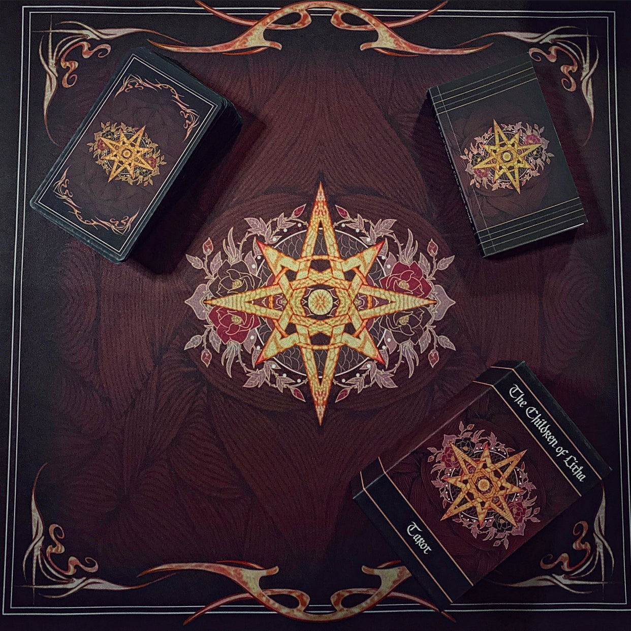 Three boxed decks of cards arranged on a dark decorative mat with a large ornate star and floral emblem in the center. The boxes are black with gold and red printed artwork and visible text including 'The Chosen of Light' and 'Erase'.