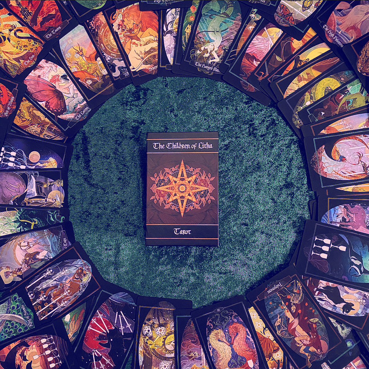 A tarot deck box titled 'The Children of Urush' sits in the center of a circular arrangement of illustrated tarot cards on a textured green surface.