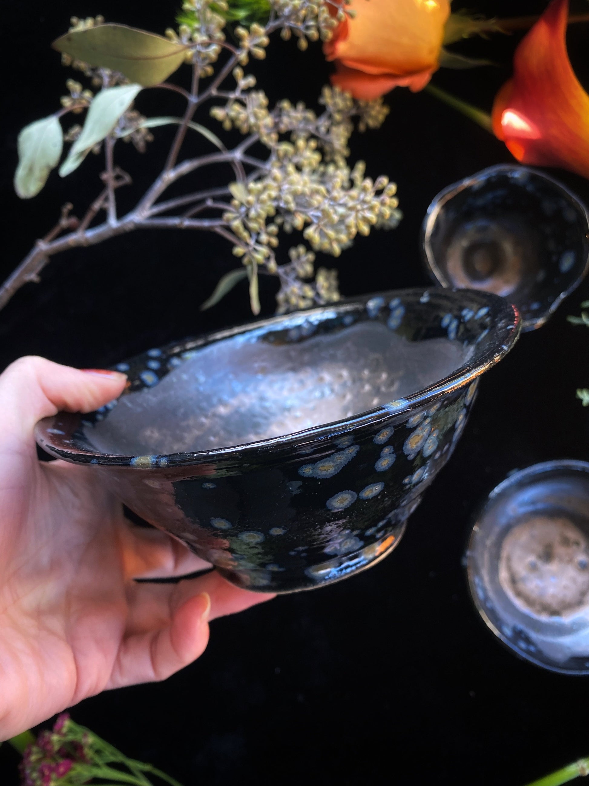 Hand holding a black ceramic bowl with white floral patterns against a dark background