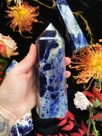 Hand holding a blue marbled crystal with flowers in the background
