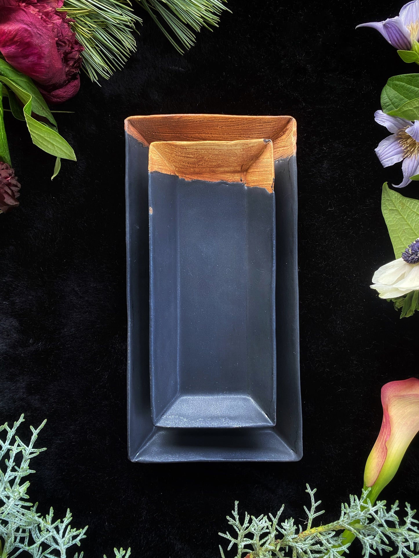 Rectangular blue dish with wooden rim on a black background with floral and greenery elements.
