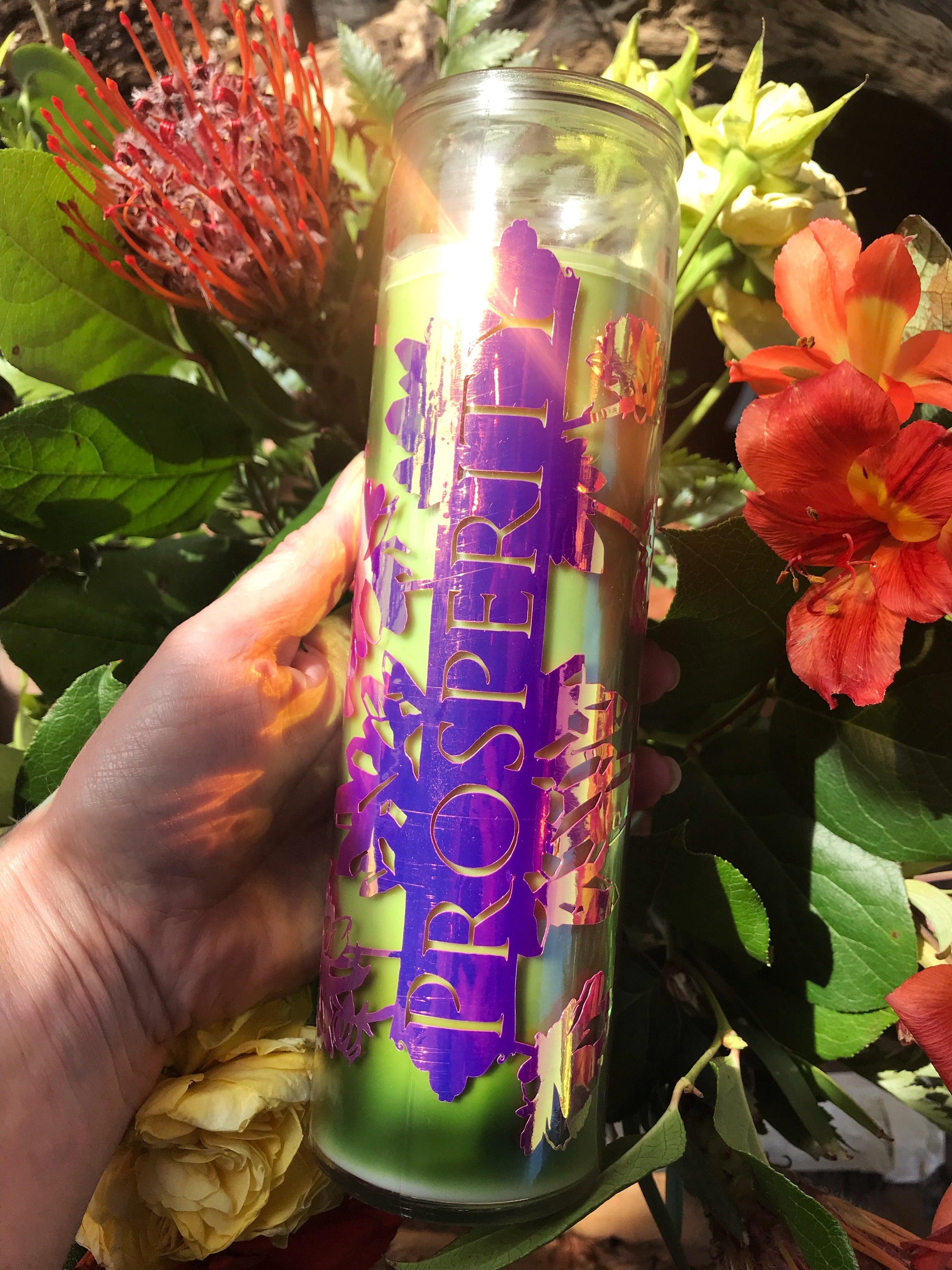 Hand holding a candle labeled 'Prosperity' among flowers