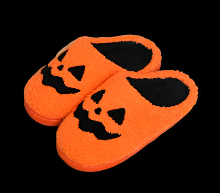 Pair of orange slippers with black jack-o'-lantern faces on a woven mat.