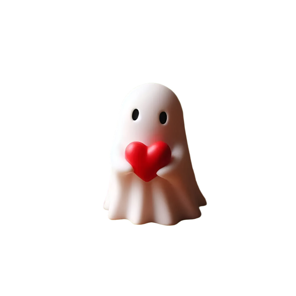 White ghost figurine holding a red heart on a wooden surface with blurred decorative elements in the background.