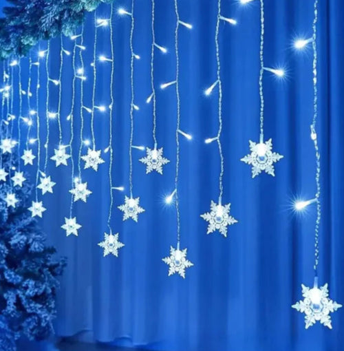 Snowflake-shaped string lights on a blue curtain with a Christmas tree in the background