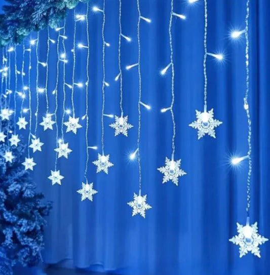 Snowflake-shaped string lights on a blue curtain with a Christmas tree in the background