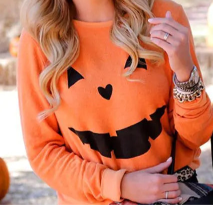Woman wearing an orange sweater with black jack-o'-lantern designs, standing in a pumpkin patch.