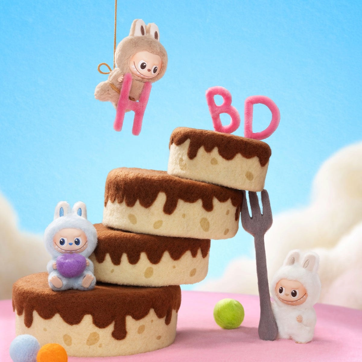 Stack of cake-shaped toys with a small Labubu plush character and 'BD' candles on a pink surface with a blue background.
