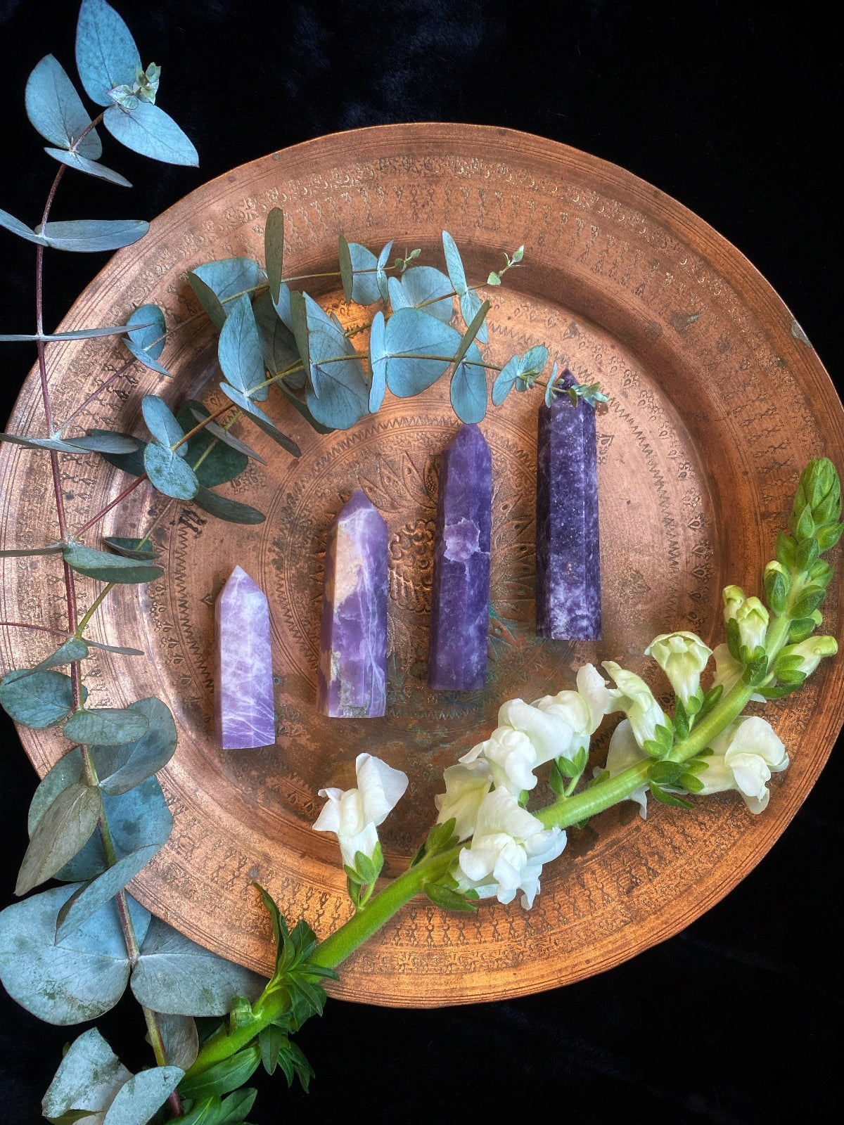 Purple crystal sticks on a wooden plate with greenery and white flowers