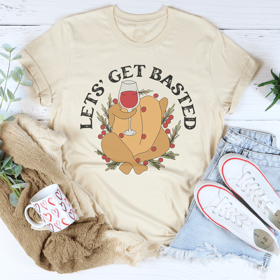 Beige t-shirt with a graphic of a turkey and 'Let's Get Basted' text, surrounded by a mug, sweater, and jeans on a white background.