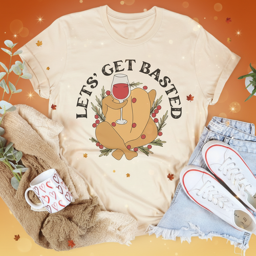 Beige t-shirt with a graphic of a turkey and 'Let's Get Basted' text, surrounded by a mug, sweater, and jeans on a white background.
