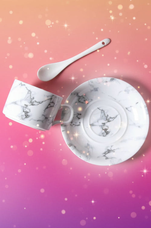 Marble-patterned ceramic cup, saucer, and spoon on a gray surface