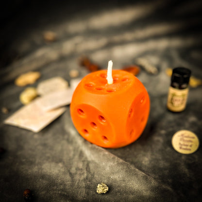 Orange dice-shaped candle on a dark surface with various small objects.