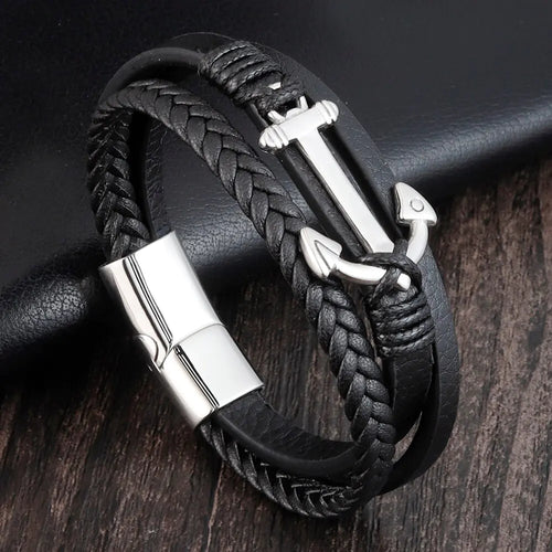 Black braided leather bracelet with silver anchor charm on a dark wooden surface