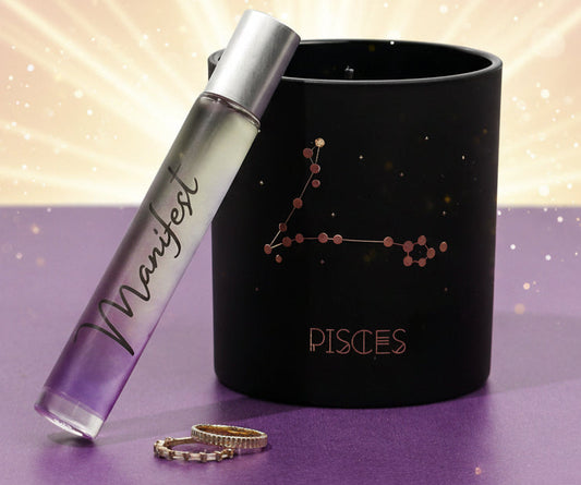 Black candle with 'Pisces' design and 'Manifest' rollerball on a purple surface.