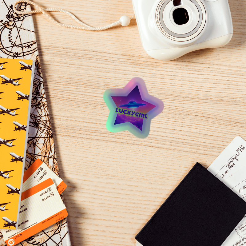 Star-shaped 'LUCKYGIRL' sticker on a wooden surface with a camera and travel-themed items.