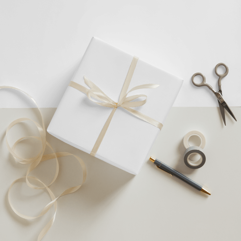 White gift box with ribbon, scissors, and tape on a light surface