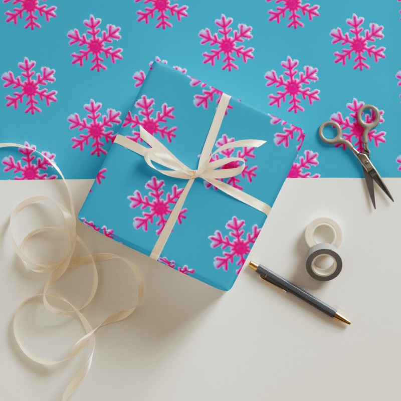 Gift box with pink snowflakes on blue background, surrounded by ribbon, scissors, and tape.