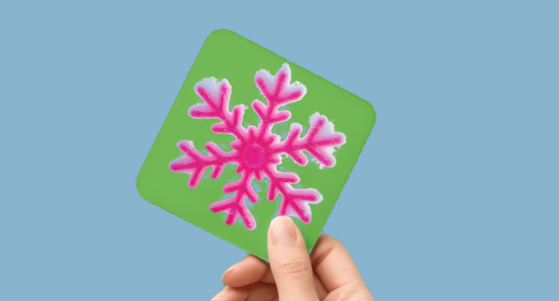 Hand holding a green card with a pink snowflake design on a white background