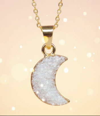 Gold necklace with a moon-shaped pendant on a white stone background