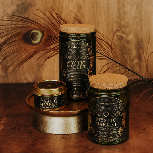 Three jars labeled 'Mystic Market' by Phantom Row on a wooden surface with peacock feathers.