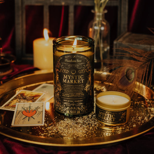 Two candles labeled 'Mystic Market' on a reflective surface with tarot cards and a vase in the background.