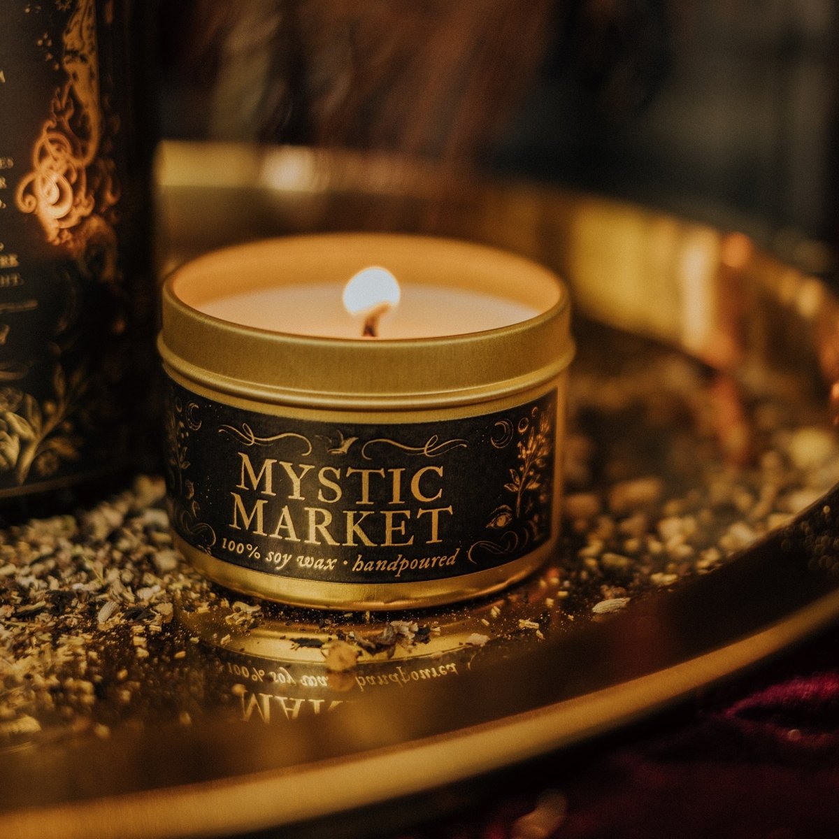 Candle in a 'Mystic Market' tin on a dark surface with a blurred background