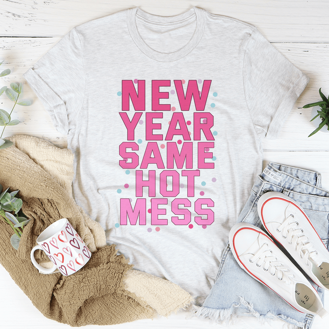 White t-shirt with 'New Year Same Hot Mess' text, surrounded by casual items on a light wooden surface.