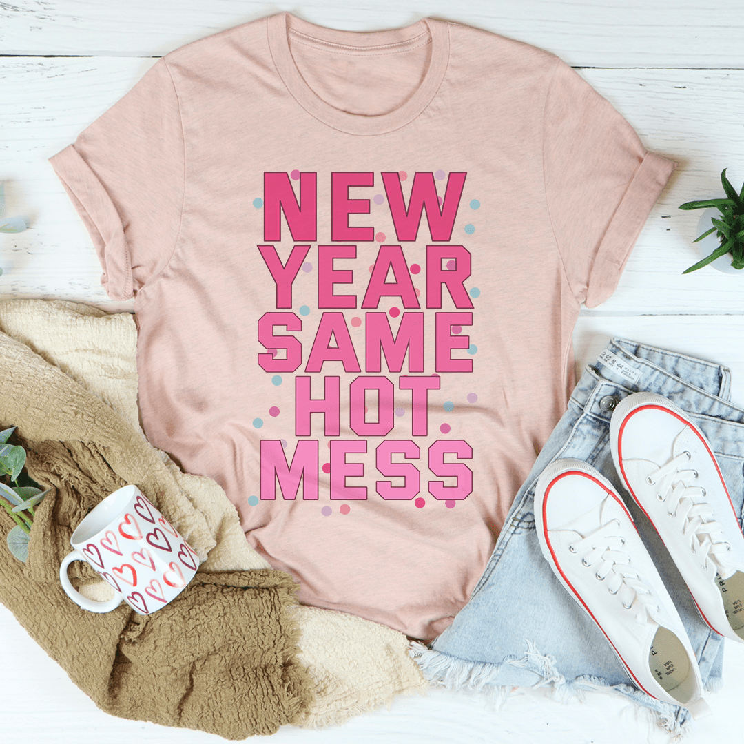 Pink t-shirt with 'New Year Same Hot Mess' text on a white surface with accessories.
