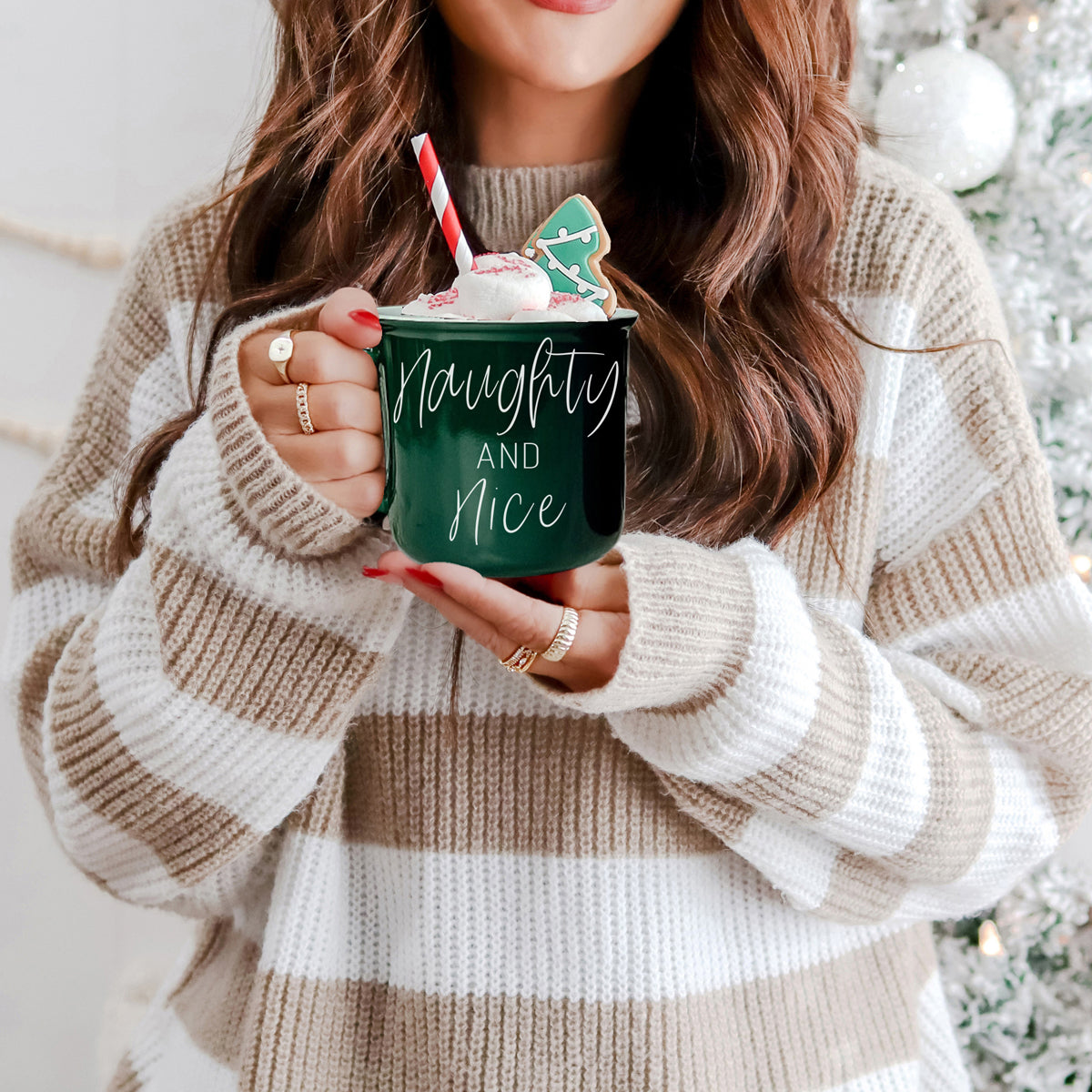 Person holding a green mug with Christmas-themed decorations, wearing a striped sweater.