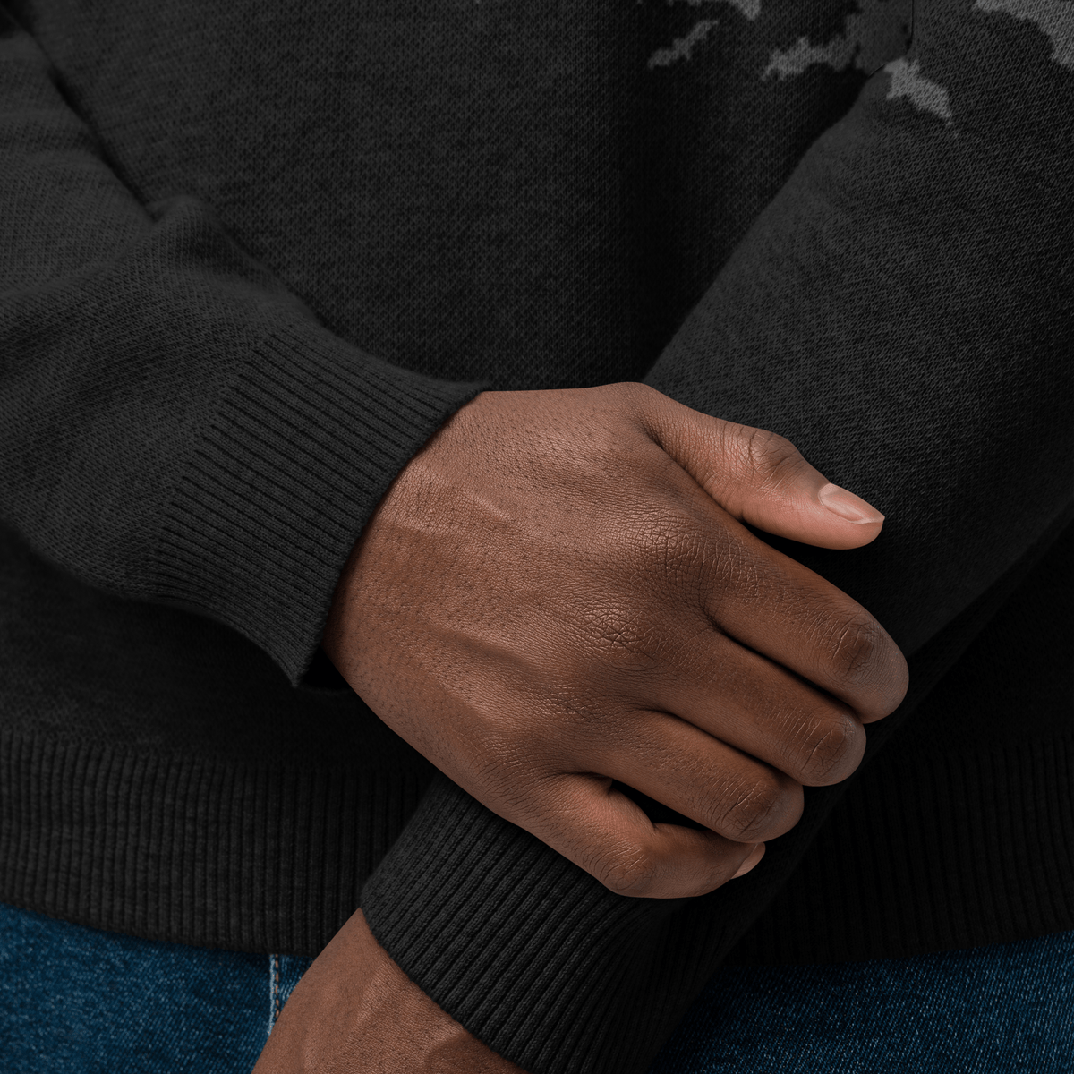 Close-up of a person wearing a black sweater with their hands clasped together.