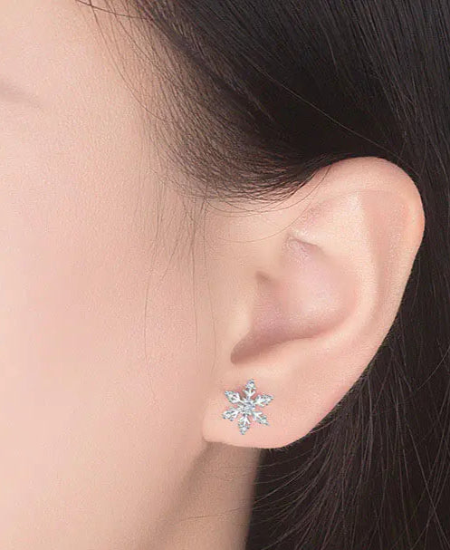 Close-up of an ear wearing a snowflake-shaped earring with a blurred background