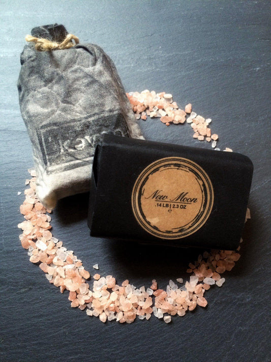 Black soap bar with 'New Moon' label on a dark surface with pink Himalayan salt crystals.
