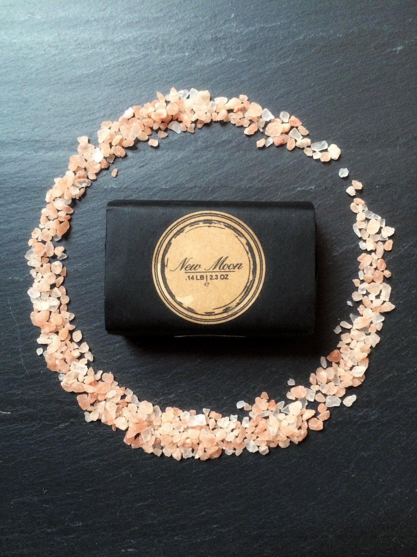 Black soap bar with gold label surrounded by small stones on a dark surface