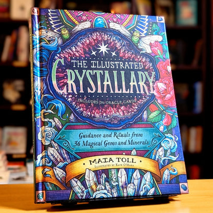 Colorful book titled 'The Illustrated Crystallary' on a wooden surface with blurred bookshelf background.