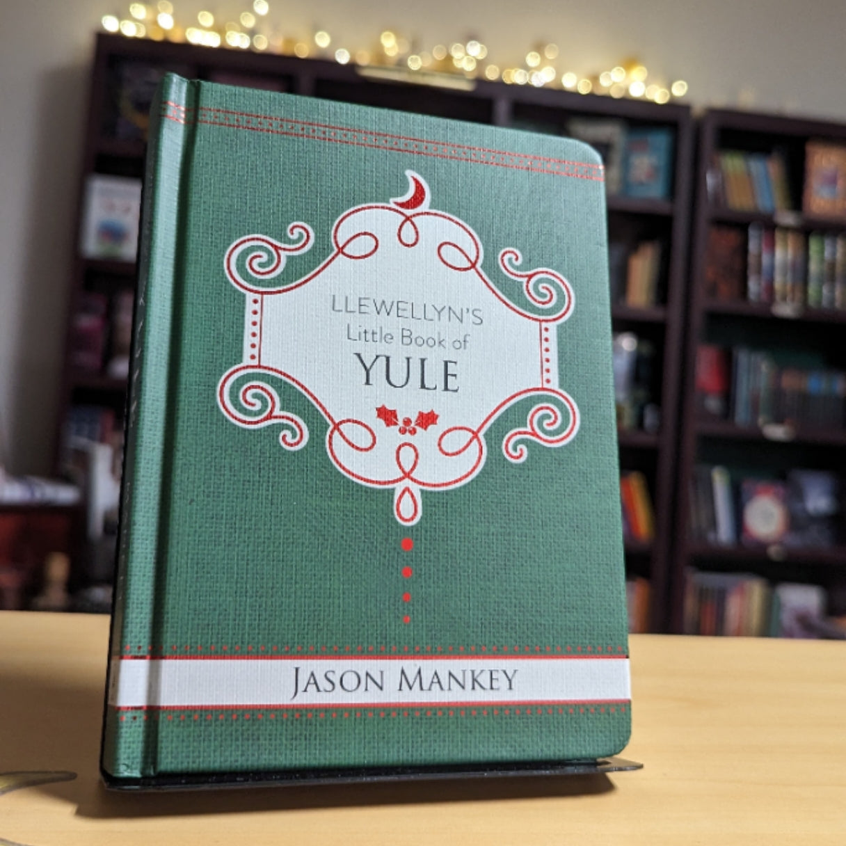 Green book titled 'Llewellyn's Little Book of Yule' by Jason Mankey on a wooden surface with a blurred bookshelf background.