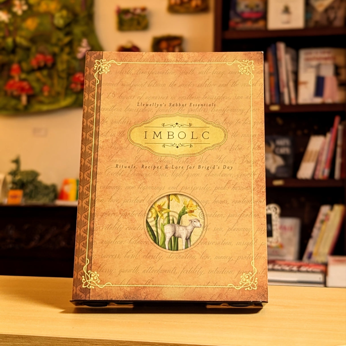 Decorative book titled 'IMBOLC' with a lamb illustration on a wooden surface.