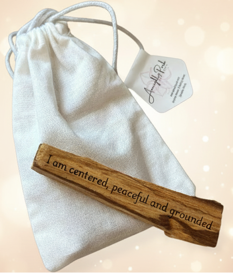 Wooden pendant with engraved text on a white drawstring bag with a tag, on a beige surface.